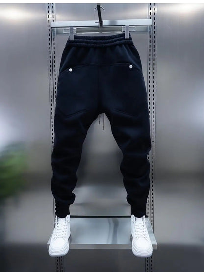 Black jogger pants on a hanger with white sneakers below against a metallic background