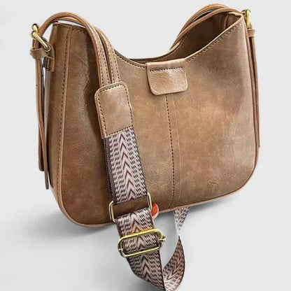 Brown leather handbag with a patterned strap on a light gray background