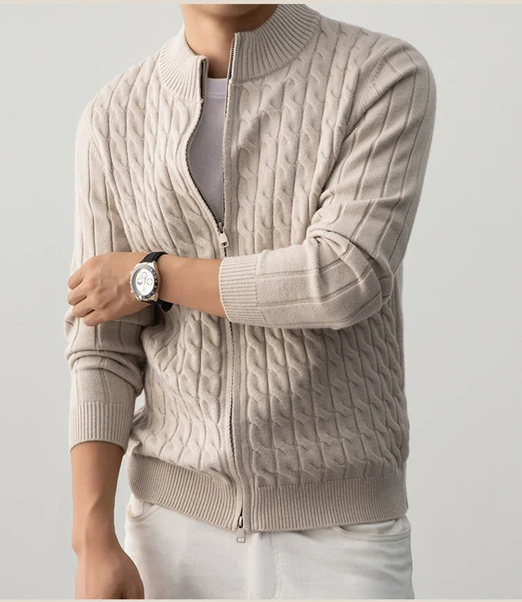 Person wearing a beige cable knit sweater with a plain background