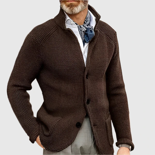 Man wearing a brown textured cardigan over a white shirt with a patterned scarf on a light gray background