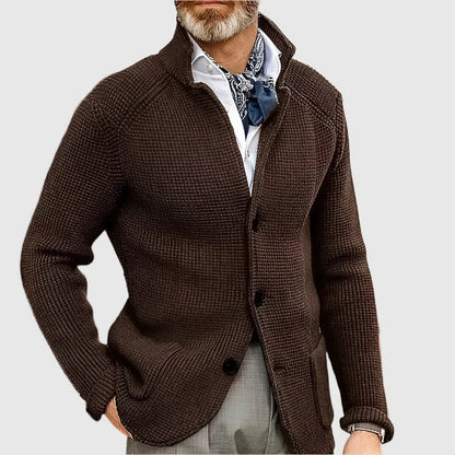 Man wearing a brown textured cardigan over a white shirt with a patterned scarf on a light gray background