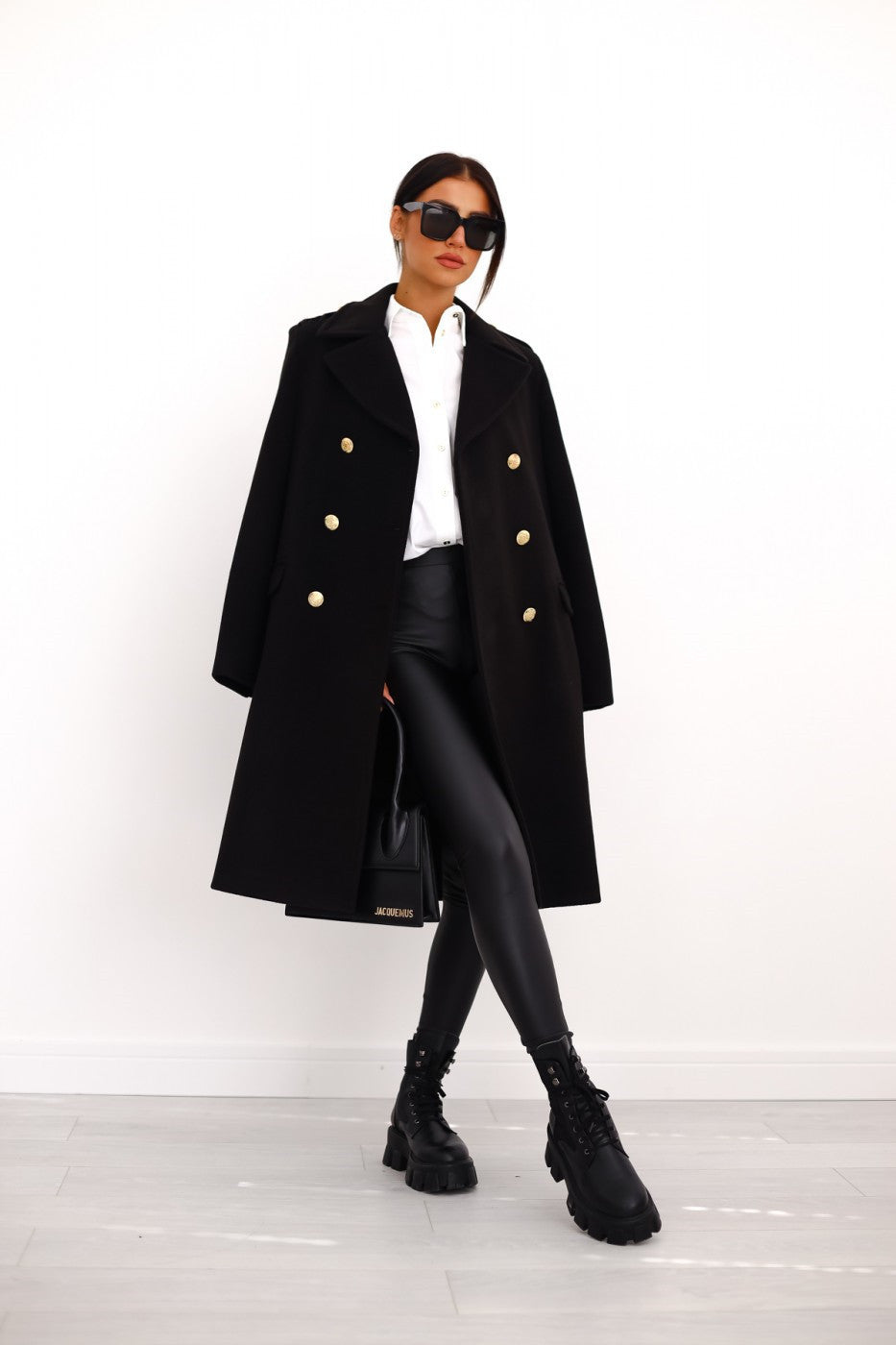 Person wearing a black coat with gold buttons on a white background