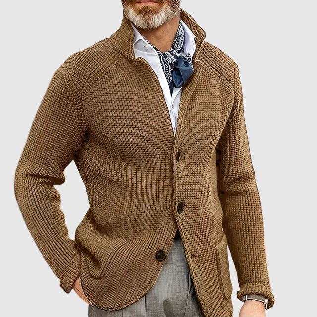 Man wearing a brown knitted cardigan over a white shirt with a patterned scarf on a light gray background