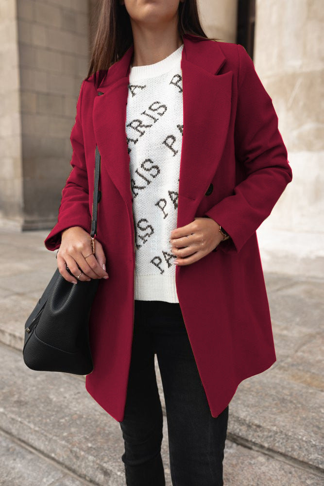 Person wearing a red coat over a white shirt with black text, holding a black handbag.