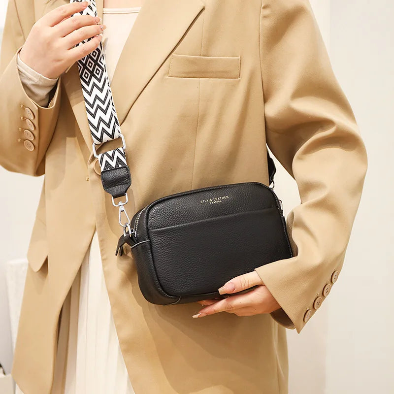 Person holding a black crossbody bag with a beige suit