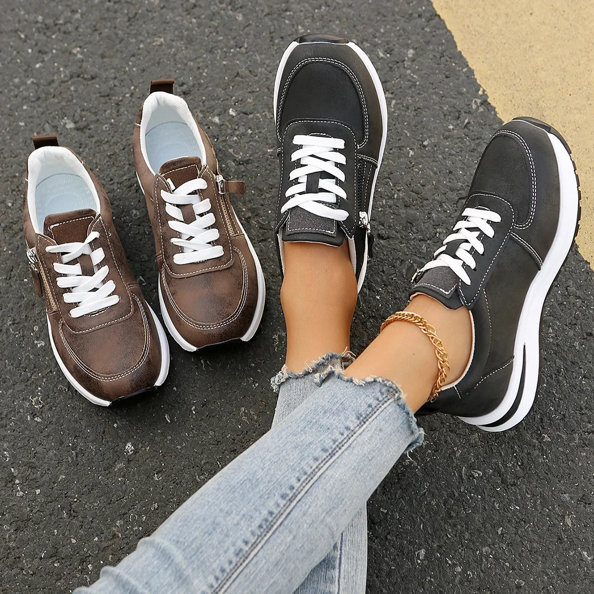 Two pairs of sneakers, one brown and one black with white soles, on a person's feet on a pavement.