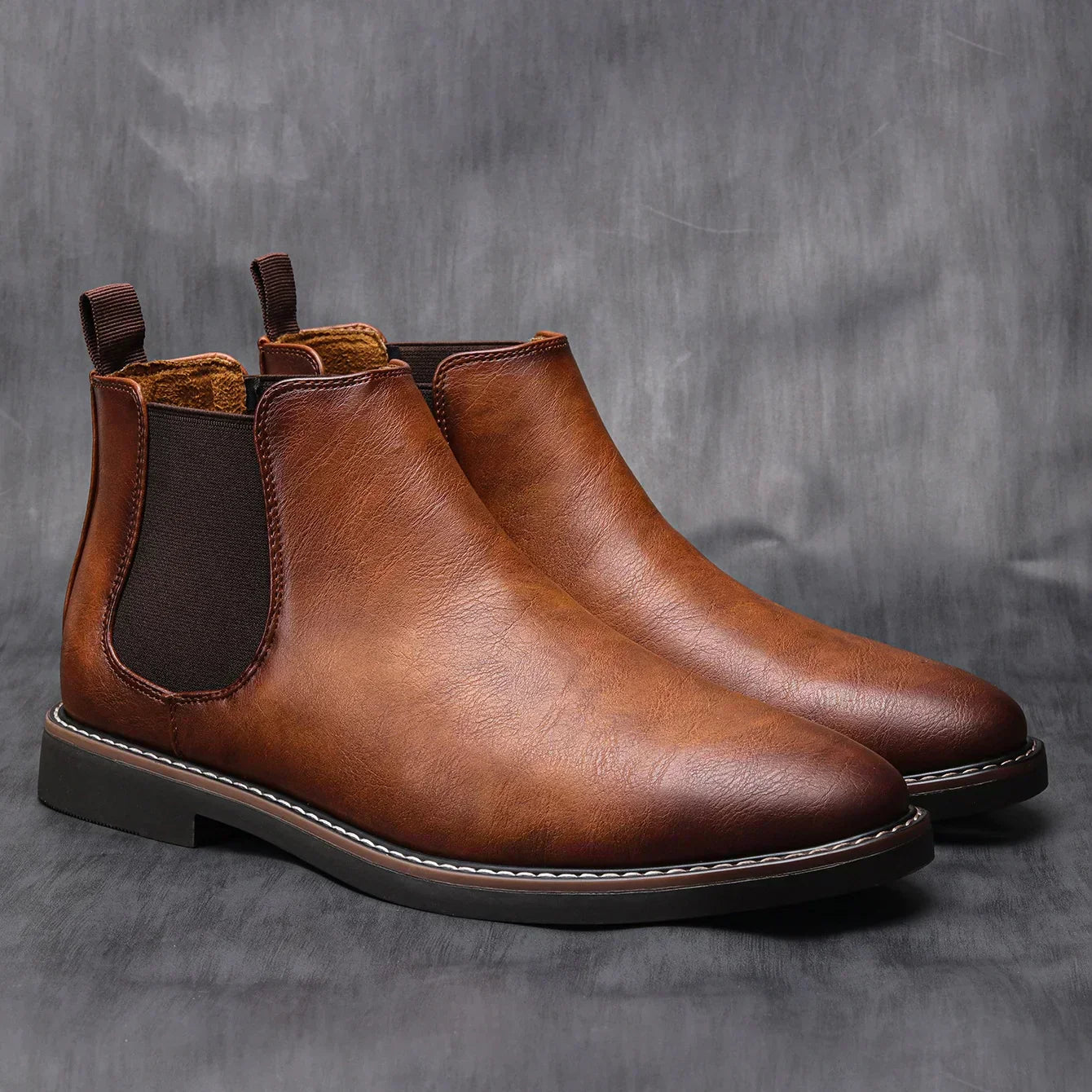 Pair of brown leather Chelsea boots on a gray background