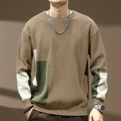 Person wearing a brown sweater with color-blocked sleeves on a neutral background