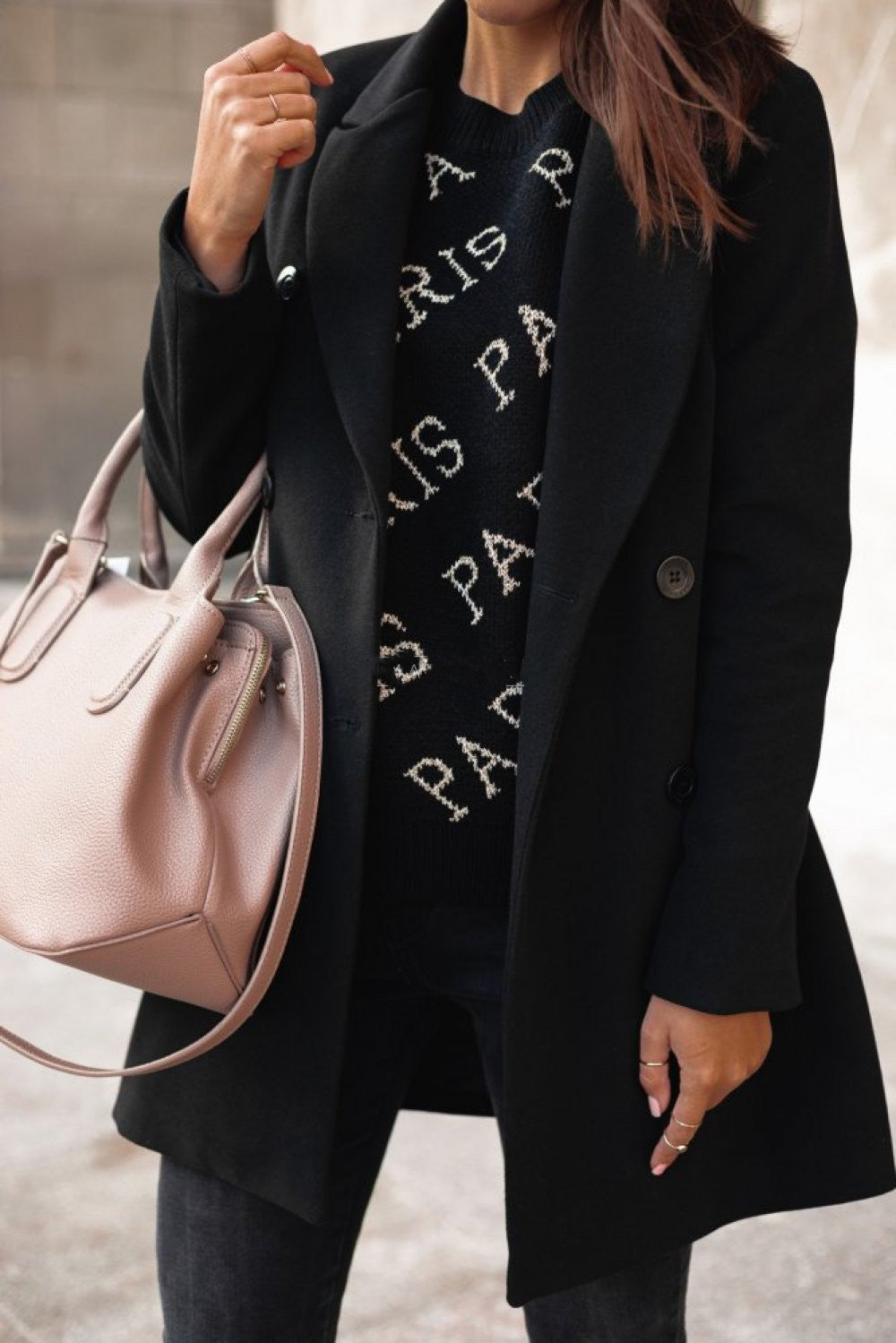Person wearing a black coat and black sweater with 'PARIS' text, holding a pink handbag.
