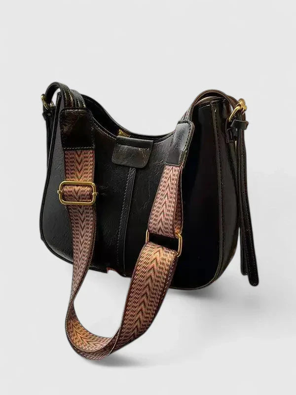 Black handbag with a patterned strap on a light gray background