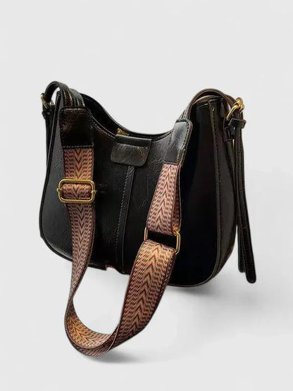 Black handbag with a patterned strap on a light gray background