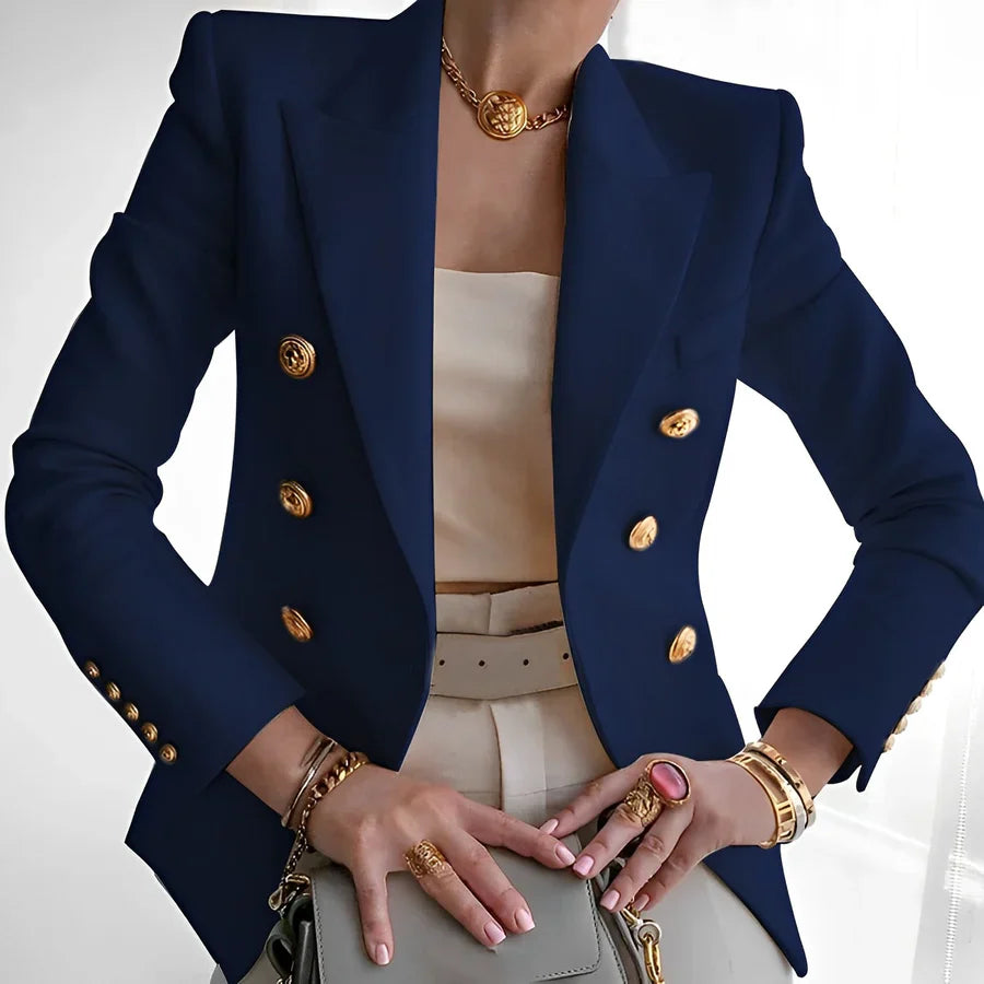 Person wearing a navy blue blazer with gold buttons, beige top, and holding a handbag.