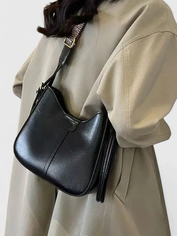 Person wearing a black leather handbag with a neutral background