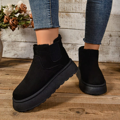 Black ankle boots worn with jeans on a wooden floor.