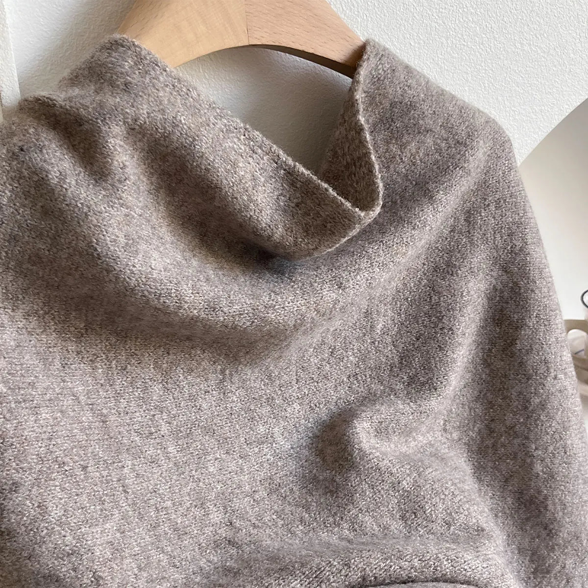 Close-up of a textured gray sweater on a wooden hanger against a white wall.