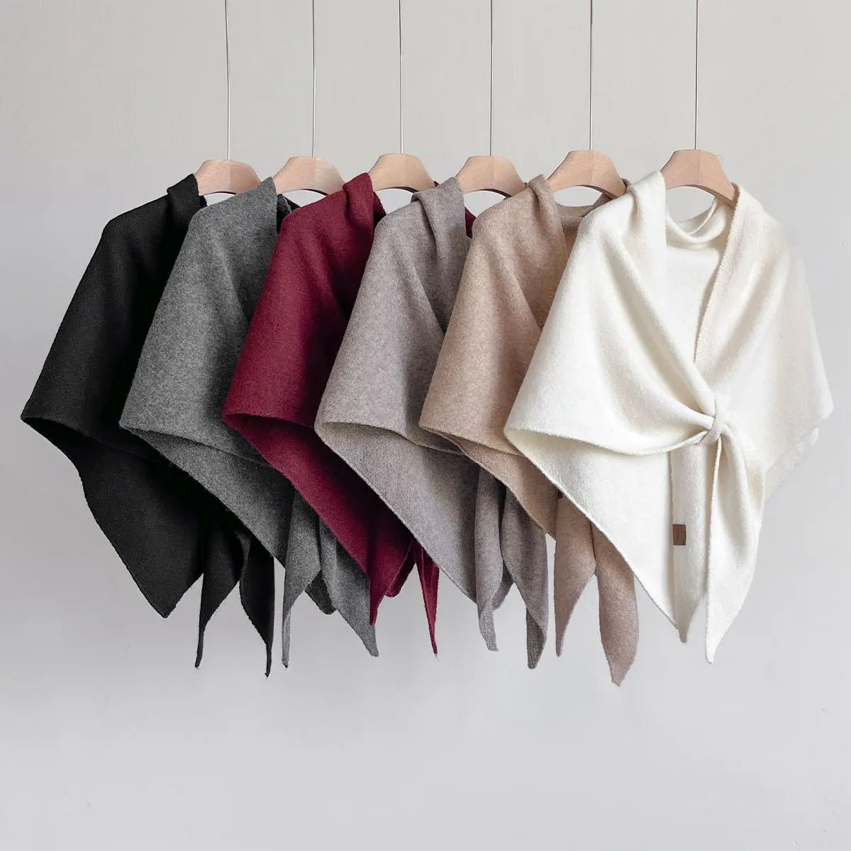 Five different colored cloaks hanging on a rack against a plain background