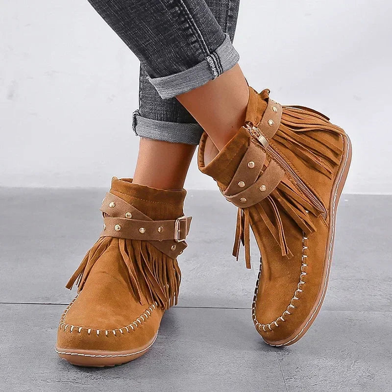 Brown suede moccasin boots with fringes worn by a person on a gray floor.