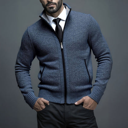 Man wearing a blue zip-up sweater over a white shirt and black tie against a gray background