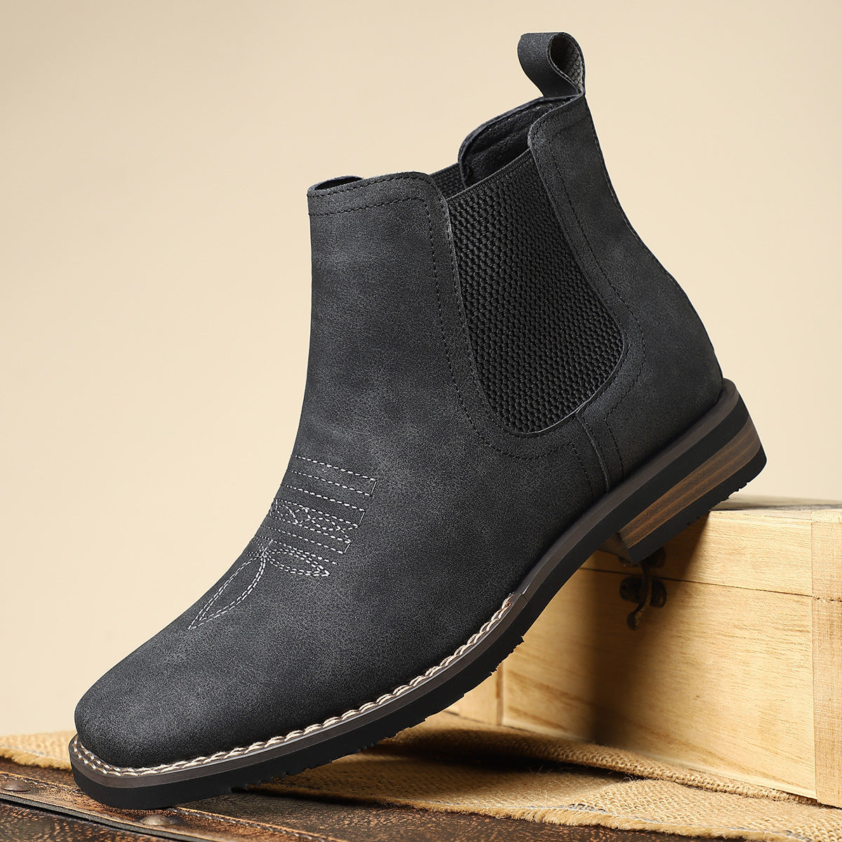 Black Chelsea boot on a wooden surface with a beige background