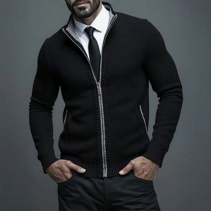 Man wearing a black zip-up sweater over a white shirt with a gray background