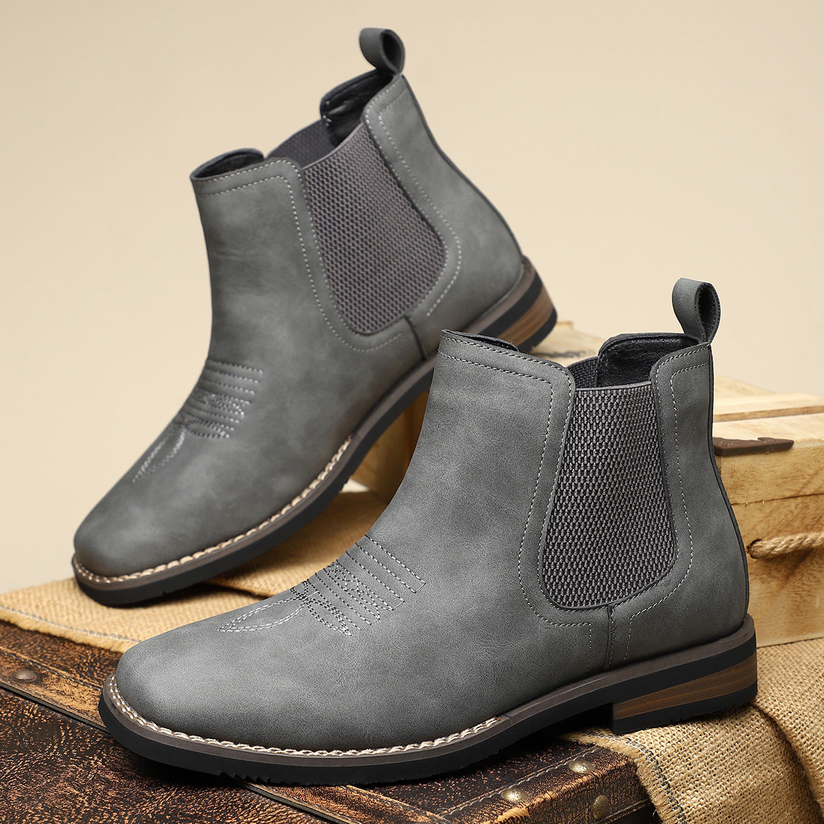 Pair of gray Chelsea boots on a wooden surface with a beige background