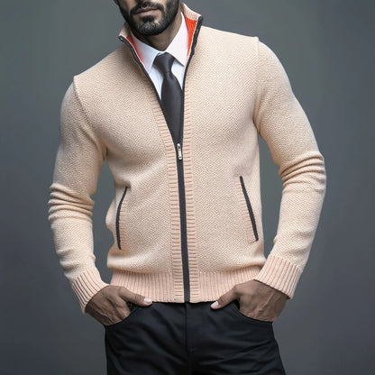 Man wearing a beige zip-up sweater over a white shirt with a black tie against a gray background