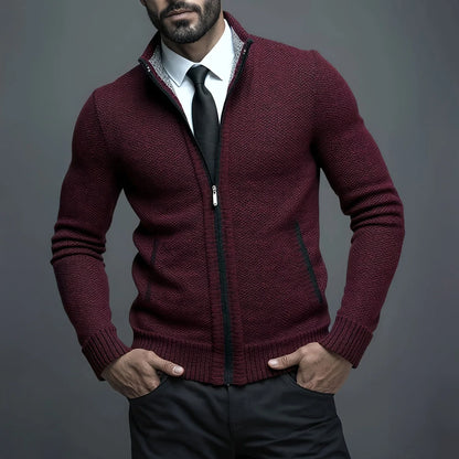 Man wearing a burgundy zip-up sweater over a white shirt with a black tie against a gray background