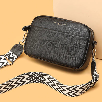 Black leather crossbody bag with a patterned strap on a beige background