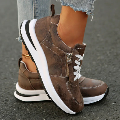 Brown sneakers with white soles worn by a person on a gray pavement.