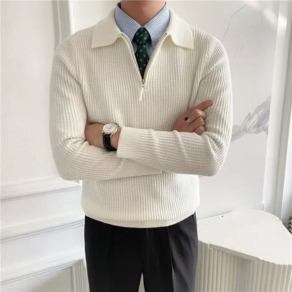 Person wearing a cream-colored sweater with a white collar, black pants, and a patterned tie.