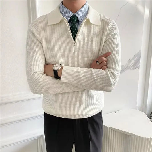 Person wearing a cream-colored sweater with a white collar, black pants, and a patterned tie.