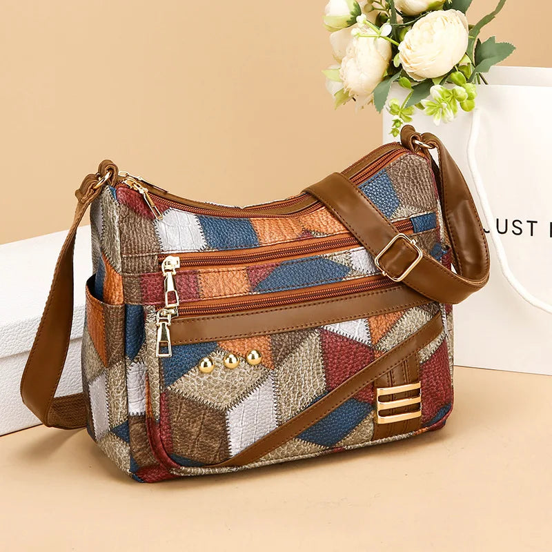 Multicolored patchwork handbag with brown leather straps on a beige surface.