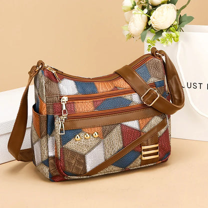 Multicolored patchwork handbag with brown leather straps on a beige surface.