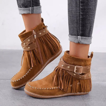 Brown suede fringe boots with buckles worn by a person on a light gray background