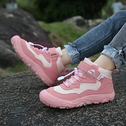 Pink hiking boots worn by a person on a rocky surface with a blurred natural background