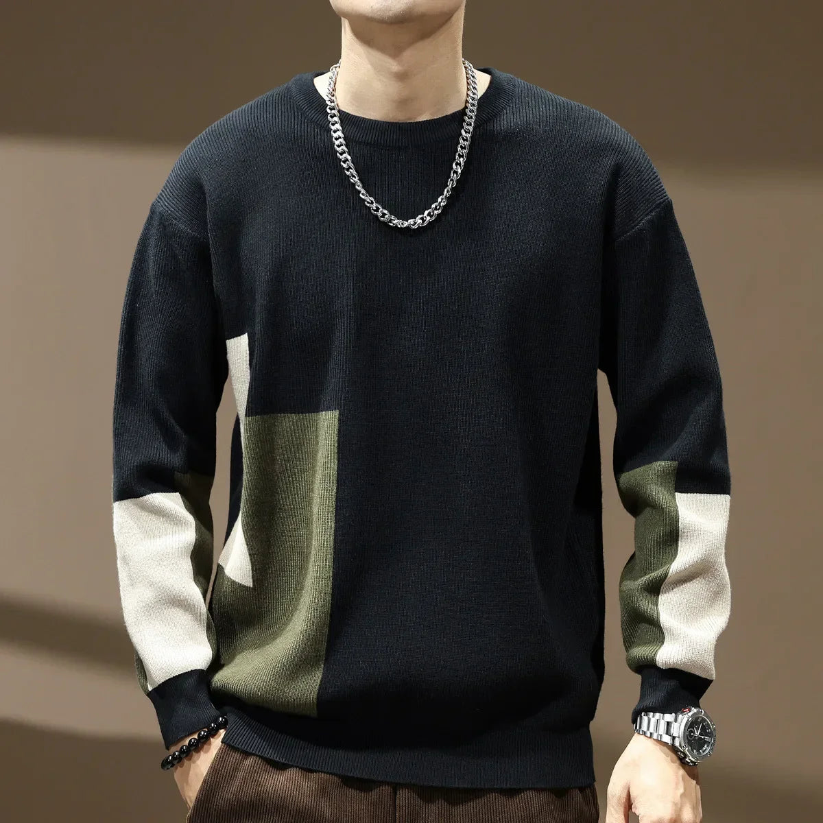 Person wearing a black, green, and white sweater with a chain necklace on a brown background