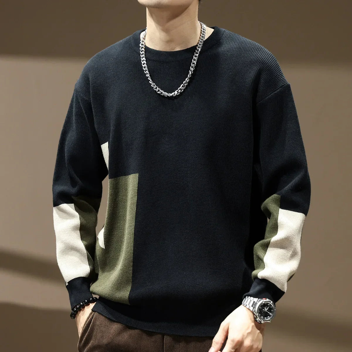 Person wearing a black, green, and white sweater with a chain necklace on a brown background