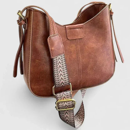 Brown leather handbag with a patterned strap on a light gray background