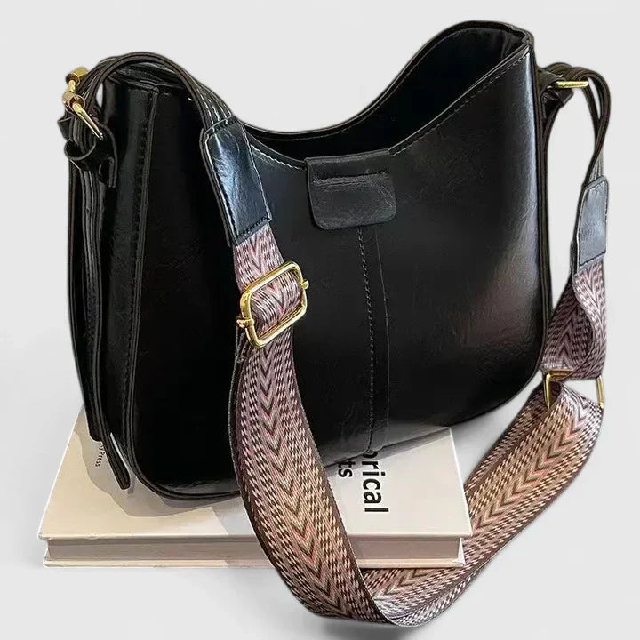 Black handbag with a patterned strap on a white background