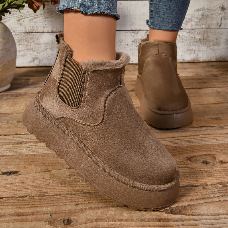Brown suede ankle boots on a wooden floor with a neutral background
