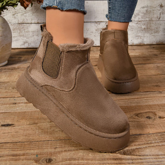 Brown suede ankle boots on a wooden floor with a neutral background