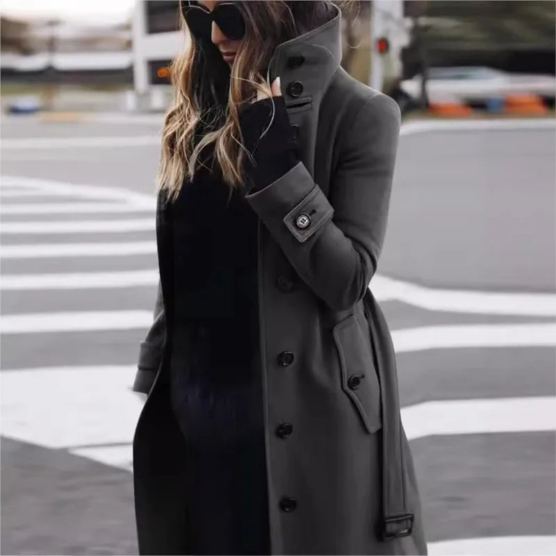 Person wearing a gray coat and black dress on a street.