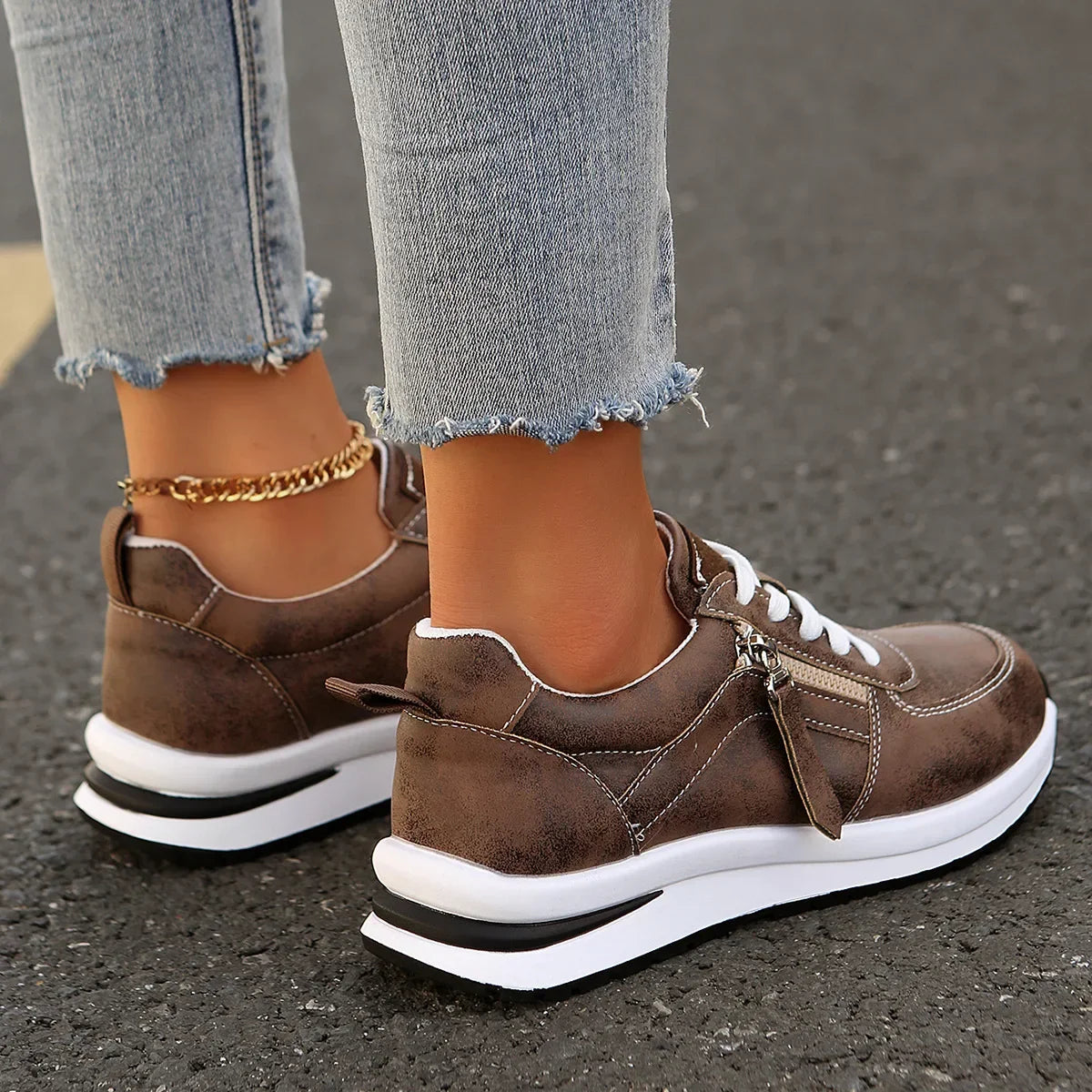 Brown sneakers with white soles worn on a dark surface
