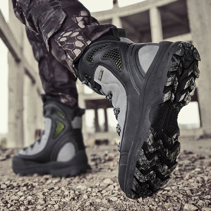 Close-up of a person wearing black tactical boots with a textured sole on a rocky surface.