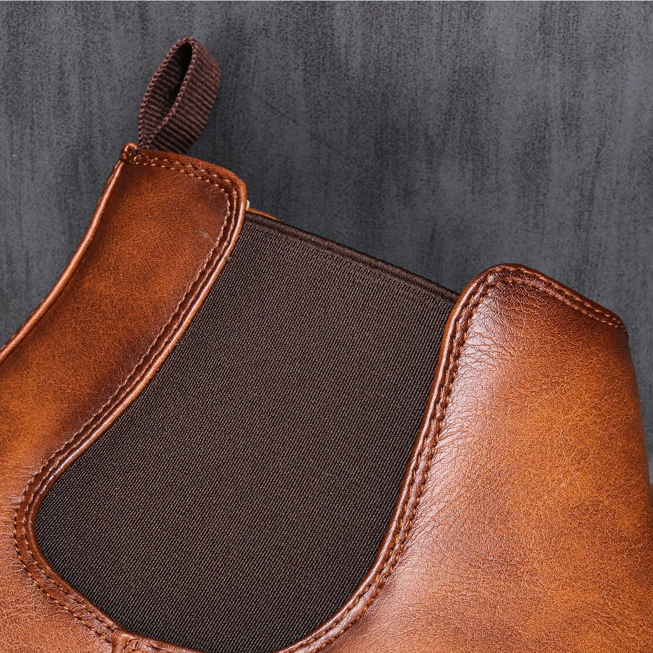 Brown leather boot with a black patch on a gray background