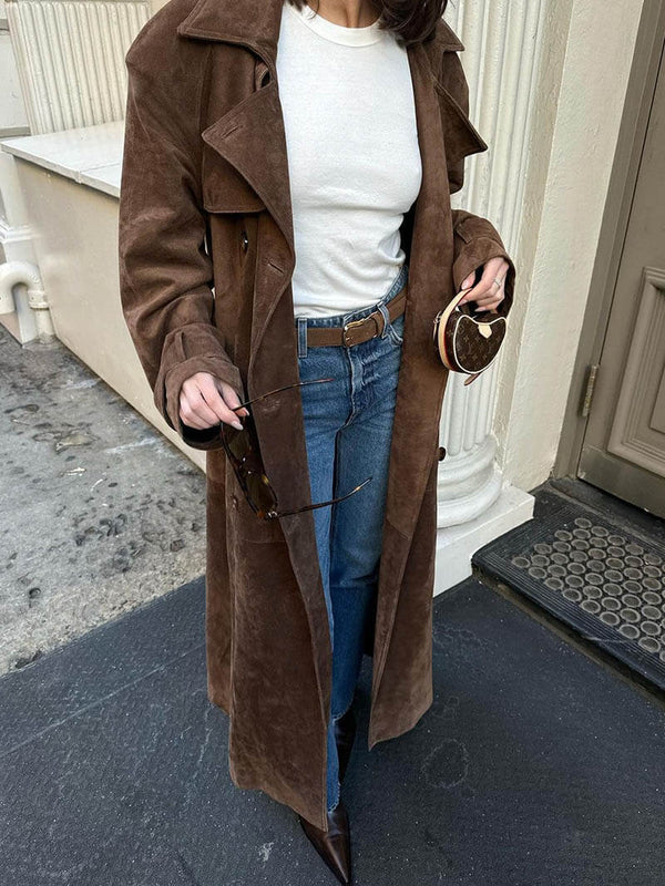 Person wearing a brown coat, white shirt, and blue jeans standing on a doorstep.