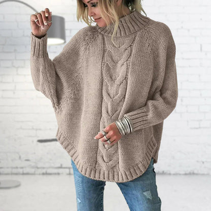 Person wearing a beige cable knit sweater with a white brick wall background