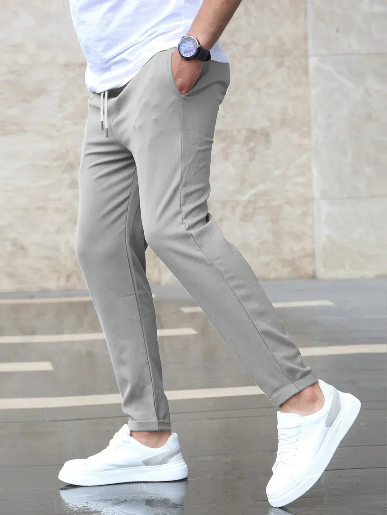 Person wearing gray pants and white sneakers against a neutral background