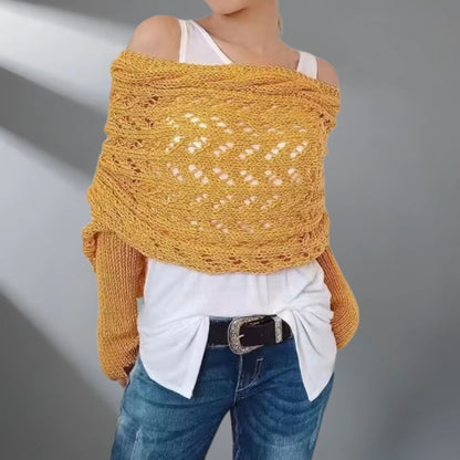 Person wearing a mustard yellow knitted shawl over a white top and blue jeans on a gray background