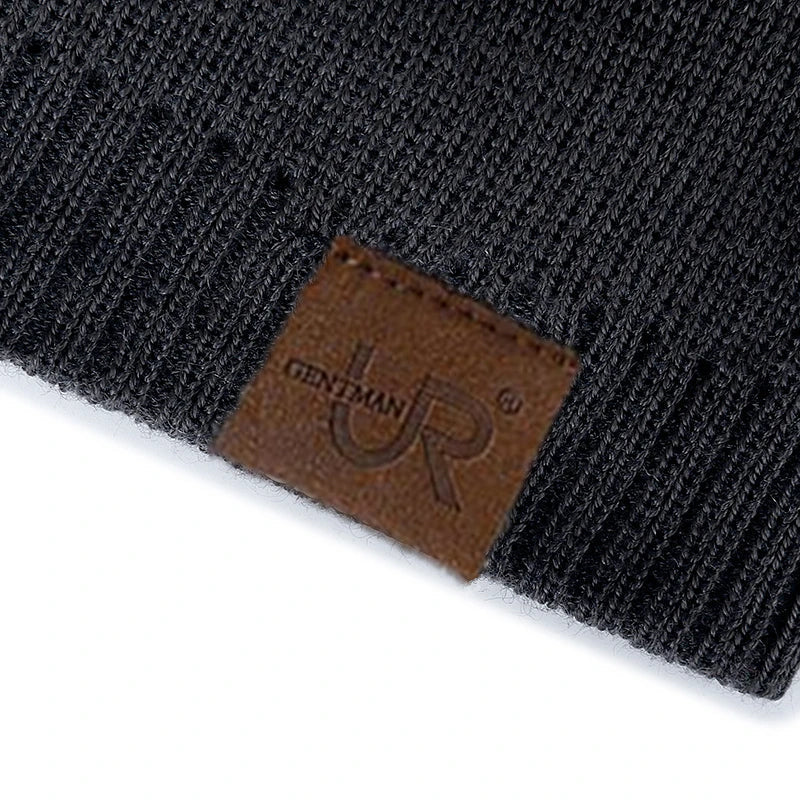 Black knit beanie with a brown leather patch featuring a logo on a white background